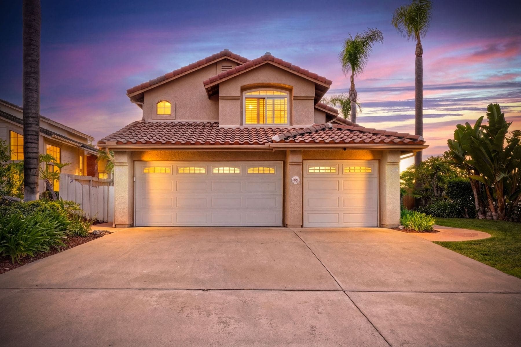 Two-story home with a tile roof photographed at twilight, garage lights on